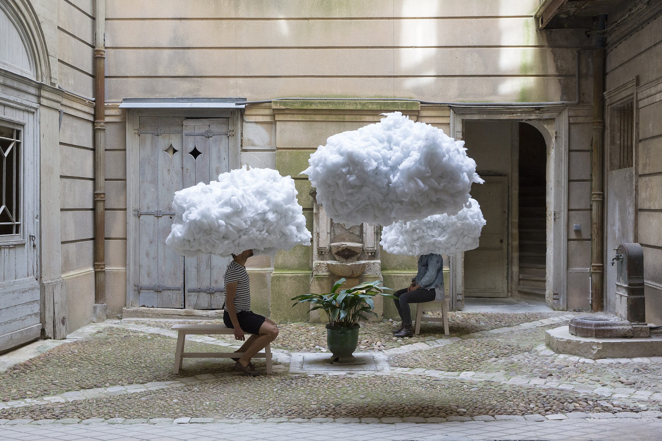 Visitors sit in a historic courtyard with their heads enclosed by suspended white cloud forms