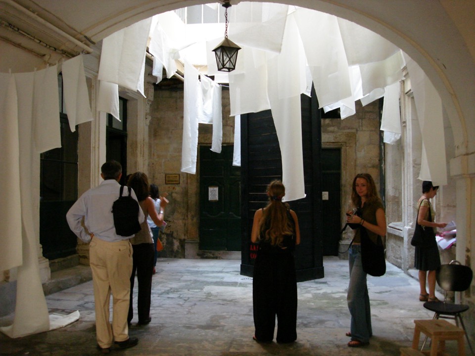 Suspended white fabric elements hanging down into the courtyard interior above the height of the visitors.
