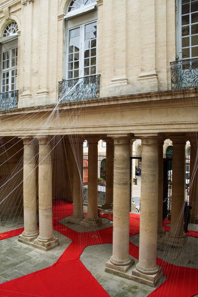 Red fabric outlining a network on the ground of the courtyard with suspended wires attached.