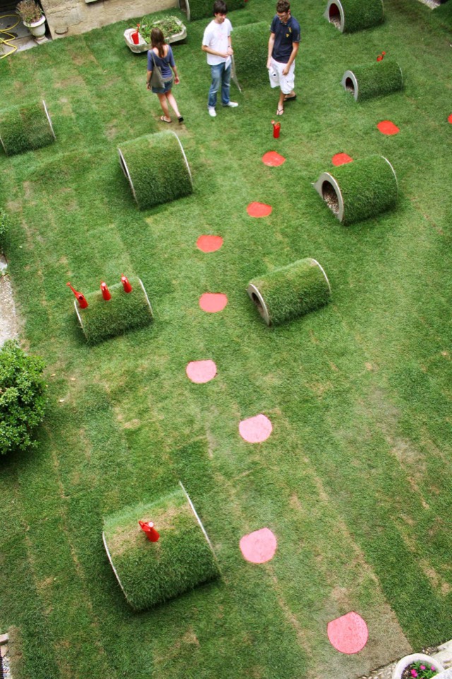 Grass sod wrapped over plastic tubing adorned with watering cans and stepping stones.