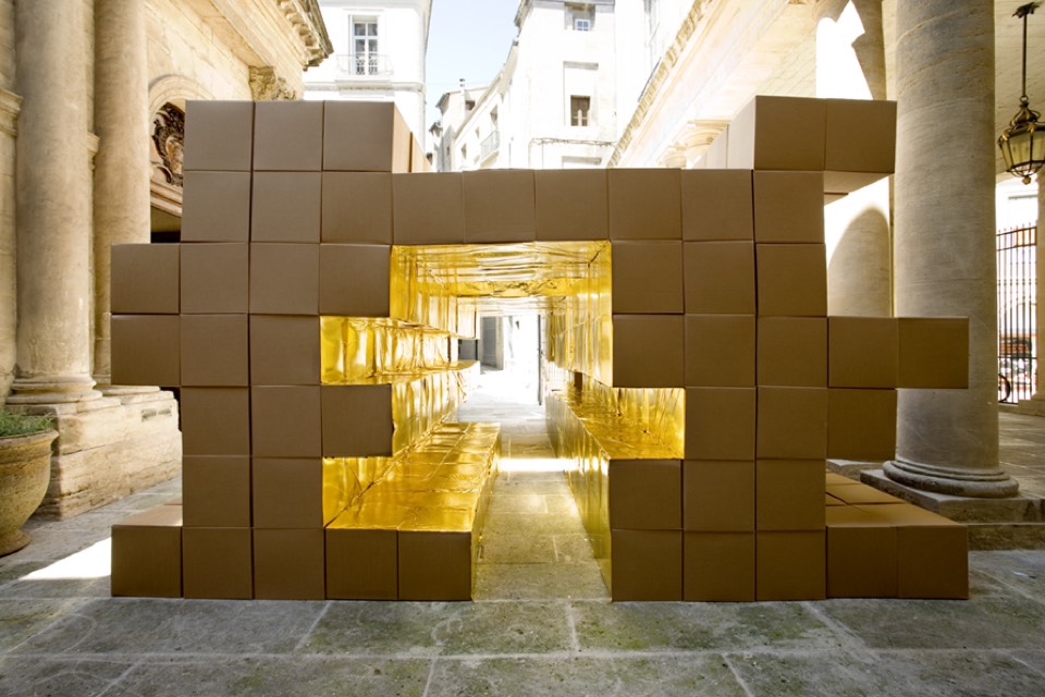 Cardboard volumes stacked to make a corridor lined with gold metallic paper.