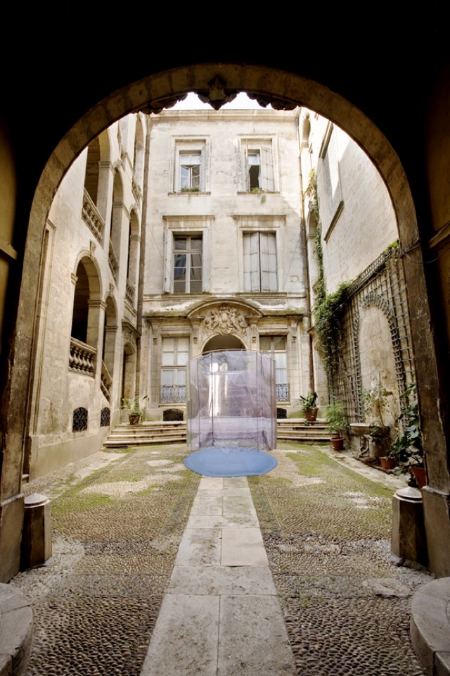Oval of printed fabric hovering over a blue carpet suspended in the center of the courtyard.